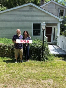 A mand and woman standing in front of house with  "sold" sign