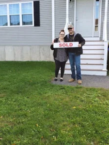 A couple standing in front of house with "sold" sign