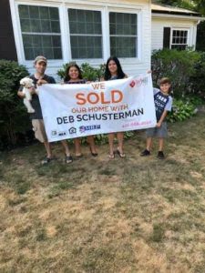 Family standing in front of house with "sold" sign