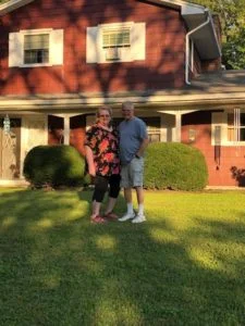 Senior couple standing in front of red house