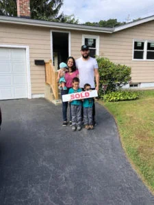 Man and woman with 3 young child holding a "sold" sign standing in front of house 