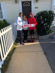 A family standing in front of house with "sold" sign